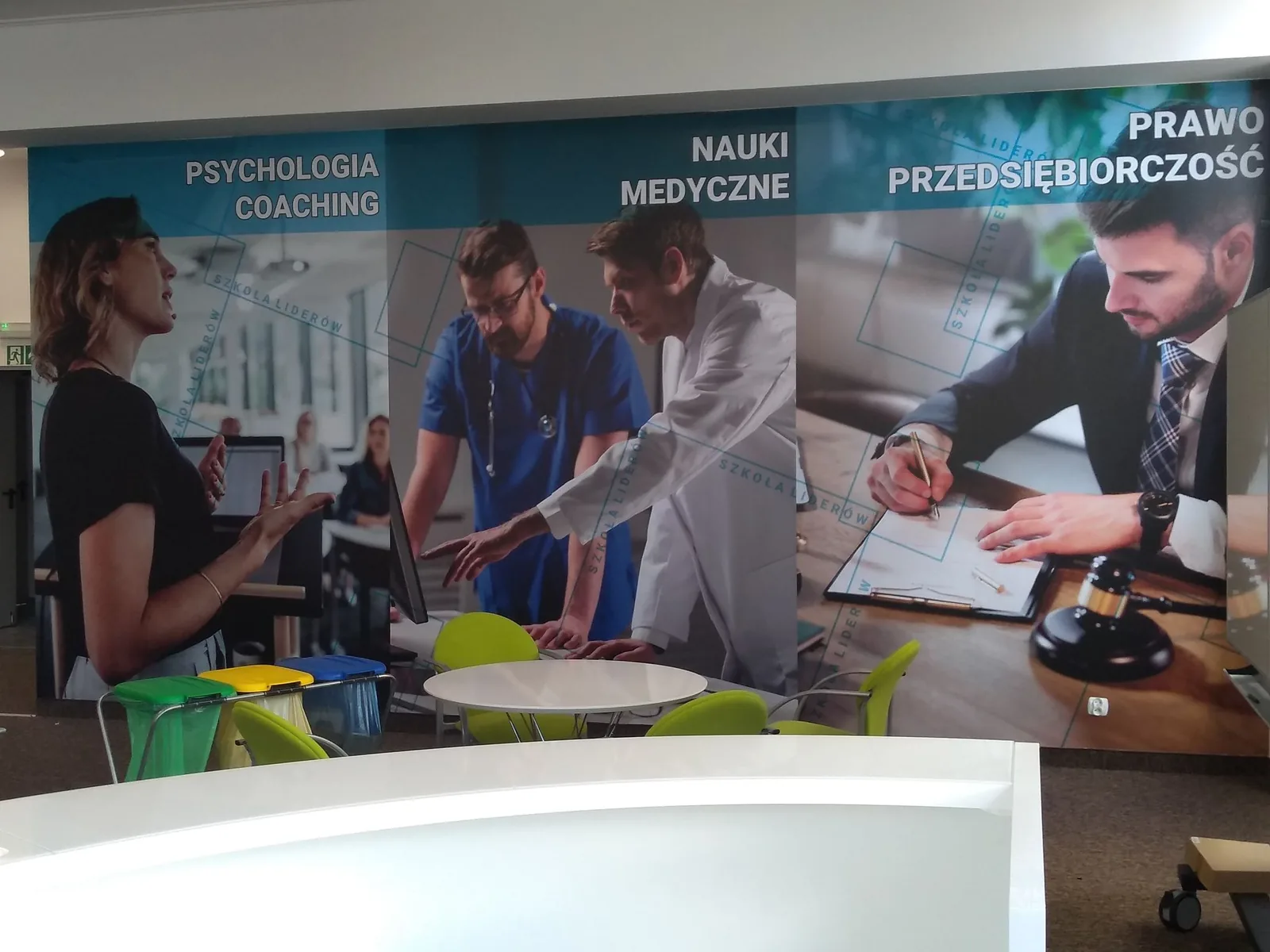 Wielkoformatowy wydruk na ścianie w strefie wejścia do biura, grafika podzielona na trzy pola tematyczne